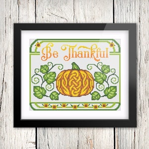 May include: A cross-stitch pattern featuring a pumpkin with a Celtic knot design, surrounded by green leaves and sunflowers. The text "Be Thankful" is written in a decorative font above the pumpkin.