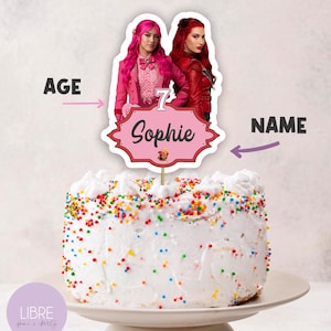 May include: A cake topper featuring two figures with bright pink and red hair, positioned above a pink scalloped sign displaying the number 7 and the name Sophie in black script. The topper is inserted into a white cake covered in colourful sprinkles.