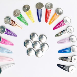 May include: A set of 18 silver metal hair clips with colourful plastic barrettes. The clips are arranged in a semi-circle with the barrettes facing outwards. The barrettes are in a variety of colours, including red, orange, yellow, green, blue, purple, pink, and white.