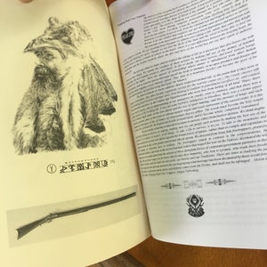 May include: Open book with a black and white illustration of a Native American man wearing a fur hat and coat. The book is titled "Wapping Heart Free Trappers". The text on the page discusses the history of the trapping trade and the importance of respecting nature and wildlife.