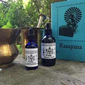 May include: Two blue glass bottles with black labels and white text. The labels read "Ashwagandha Withania Somnifera Full Spectrum Spagyric Tincture 4 Oz. Rasayana Ausadhi". The bottles are sitting on a grey surface.