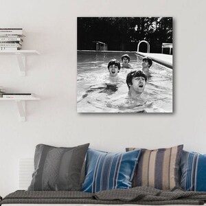 Puede incluir: Impresi&oacute;n en blanco y negro enmarcada de The Beatles en una piscina. Los miembros de la banda est&aacute;n en el agua, con sus rostros mostrando alegr&iacute;a. La imagen est&aacute; montada en una pared blanca sobre una mesa de centro de madera y cojines.