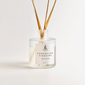Può includere: Un diffusore a lamelle in vetro trasparente con lamelle di legno. L'etichetta recita "CRACKLING FIRESIDE" e "REED DIFFUSER". Il peso netto è di 113 g. Il prodotto è progettato per aggiungere profumo a una stanza.