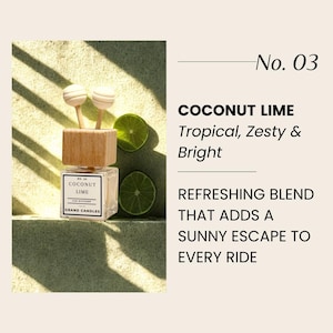 Puede incluir: Un ambientador para coche con una parte superior de madera y dos difusores blancos en forma de bola. La etiqueta dice "COCONUT LIME" y "GRAND CANDLES". Rodajas de lima se colocan cerca del ambientador. El texto dice "Tropical, Zesty & Bright."