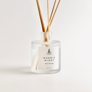 Puede incluir: Un difusor de varillas de vidrio esmerilado con varillas de madera. La etiqueta dice "NORDIC NIGHT REED DIFFUSER" y "NET WT 4 OZ". La botella tiene forma redonda y cuello estrecho. Las varillas son de color marrón claro.