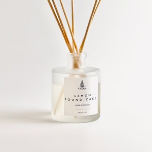 Könnte beinhalten: Ein Diffusor mit Holzstäbchen in einem Milchglasbehälter. Auf dem Etikett steht "Lemon Pound Cake" und "Reed Diffuser". Die Flasche enthält eine hellgelbe Flüssigkeit. Das Nettogewicht beträgt 113 Gramm.