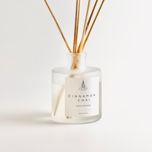 May include: A clear glass reed diffuser bottle with wooden reeds. The label reads "Cinnamon Chai Reed Diffuser" and "Net wt 4 oz". The bottle contains a light-colored liquid. The product is from Grand Candles.