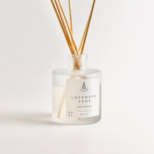 May include: A clear glass bottle with a white label that reads "Lavender Sage Reed Diffuser" and "No. 03" with a small candle graphic. The bottle is filled with a clear liquid and has wooden sticks sticking out of the top.
