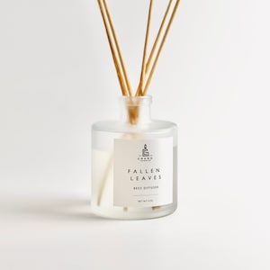 Puede incluir: Un difusor de caña de vidrio transparente con cañas de madera. La botella tiene una etiqueta blanca con el texto "FALLEN LEAVES" y "REED DIFFUSER". La botella contiene un líquido transparente y está etiquetada como "NET WT 4 OZ".