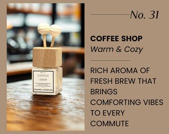 May include: A square glass car diffuser with a wooden top and two white wooden sticks. The label reads "COFFEE SHOP" and "GRAND CANDLES". The text on the image says "Warm & Cozy" and describes the aroma of fresh brew.