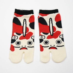 May include: A pair of white tabi socks with a red and black cartoon frog design. The socks have a split toe.