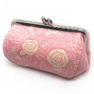 May include: A pink fabric coin purse with a floral pattern of white roses and leaves. The purse has a silver metal clasp.