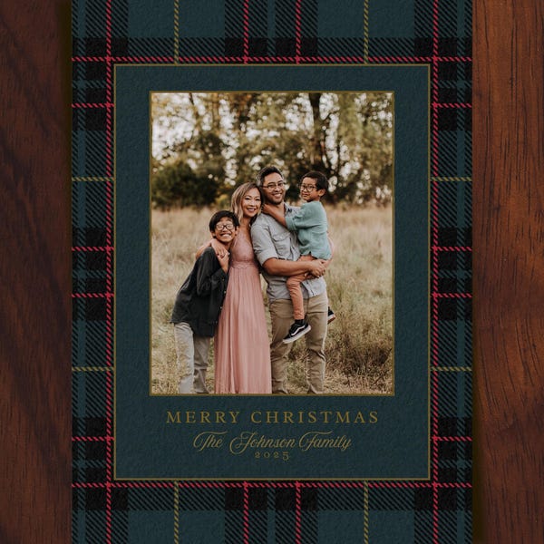 May include: A rectangular holiday card featuring a dark green and black plaid border with thin red and gold lines. The centre displays a photograph of a family of four. Below the photo, gold text reads MERRY CHRISTMAS, The Johnson Family, 2025.