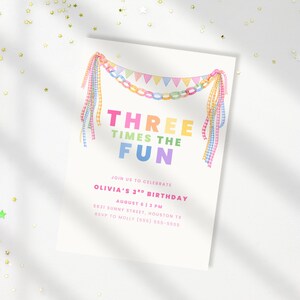 May include: A white birthday invitation card with the words "THREE TIMES THE FUN" in bright colours. The card has a decorative banner and ribbons. The text "Olivia's 3rd Birthday" is also included.