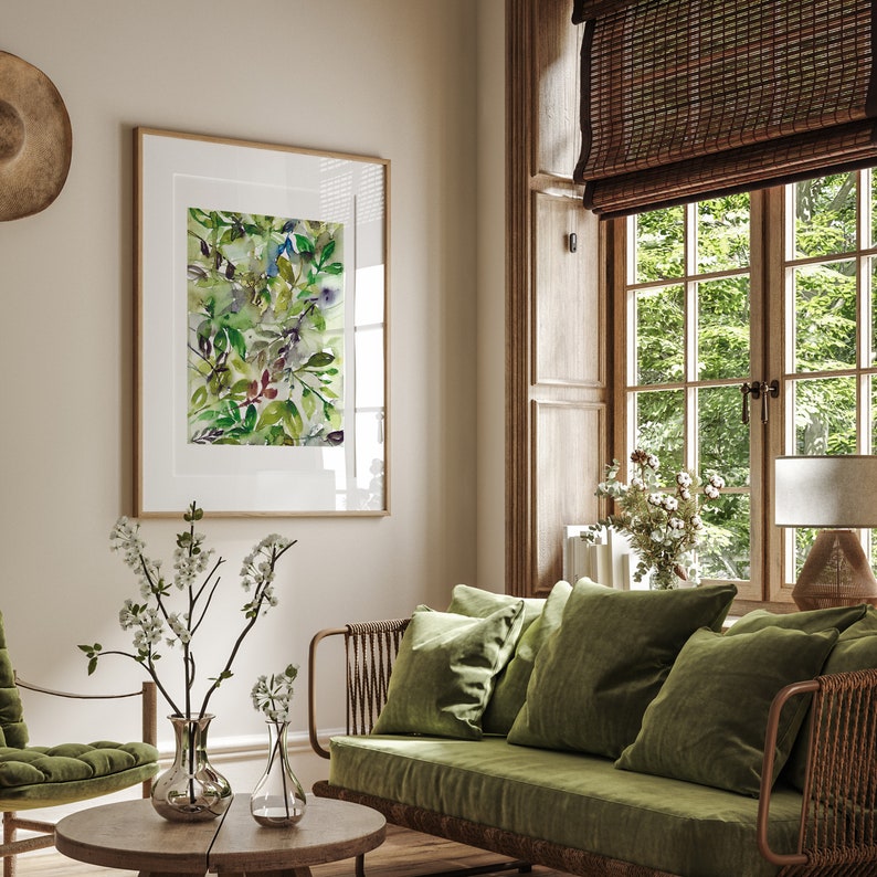 May include: A living room with a green velvet sofa, a wooden coffee table, and a framed watercolor painting of green leaves. The room has a large window with a wooden blind and a view of trees outside.