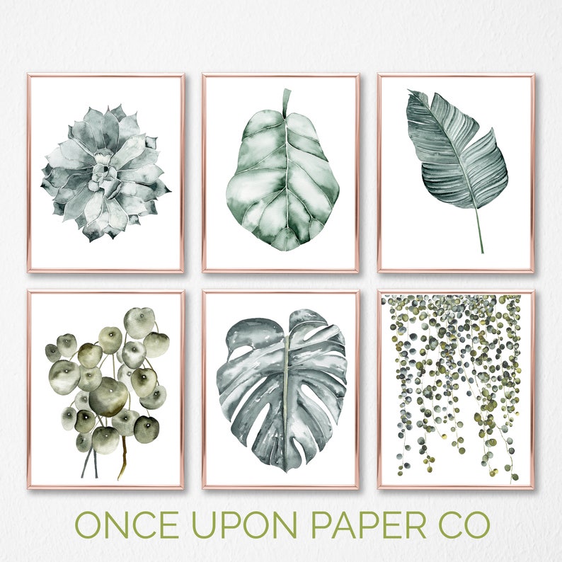 May include: Set of six watercolor prints featuring various green foliage, including a succulent, monstera leaf, palm leaf, and string of pearls. The prints are framed in a thin, gold-colored frame.