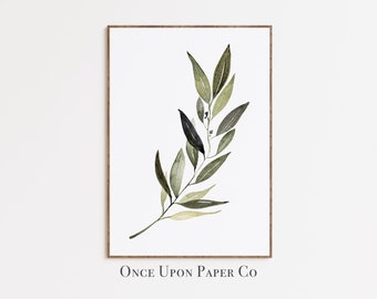 May include: A framed print featuring a watercolor illustration of a botanical sprig with green and olive-colored leaves. The artwork is set against a white background and framed in a brown wooden frame. The text "Once Upon Paper Co" is printed at the bottom.