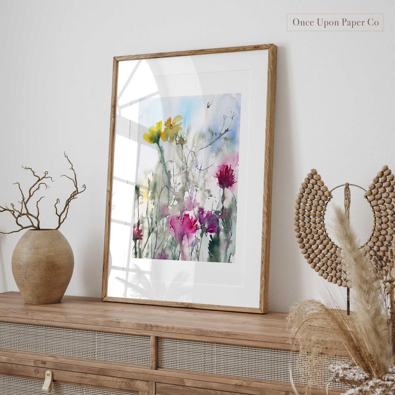 May include: Watercolor painting of a floral bouquet with yellow, pink, and purple flowers. The painting is framed in a natural wood frame and is hanging on a wall.