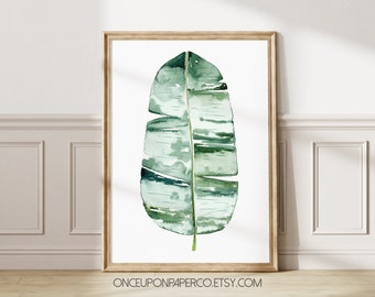 May include: A watercolor painting of a single green banana leaf in a wooden frame. The leaf is depicted in a light green and dark green color scheme. The background is white. The text "ONCEUPONPAPERCO.ETSY.COM" is at the bottom of the image.