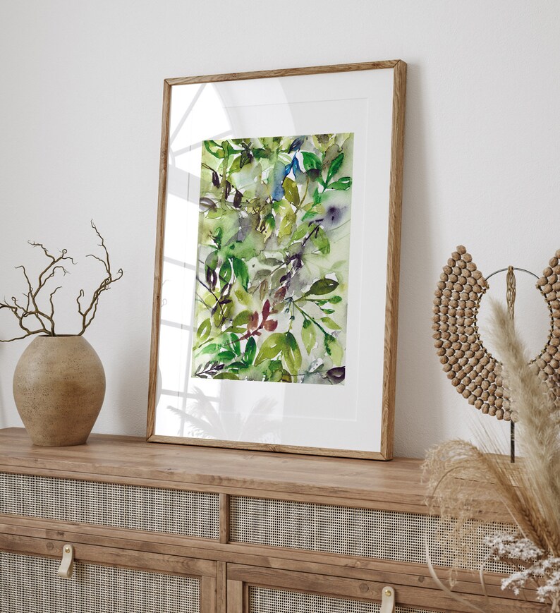 May include: A framed watercolor painting of green and blue leaves in a wooden frame. The painting is on a wooden shelf with a vase of dried branches and a wooden beaded necklace.
