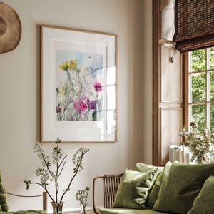 May include: A framed watercolor painting of pink and yellow flowers in a field. The painting is in a light wood frame and is hanging on a light beige wall.