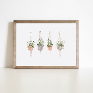 Peut inclure: Impression aquarelle encadrée de quatre plantes suspendues dans des macramés. Les pots sont de couleurs pêche, grise et beige. L'œuvre est encadrée dans un cadre en bois brun clair, idéale pour une touche naturelle.