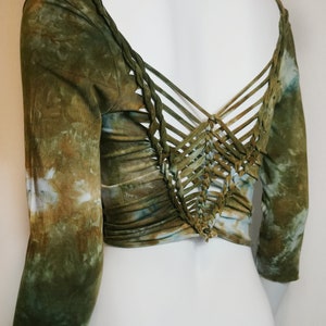 Könnte beinhalten: Ein langärmliges Crop-Top in Grün-, Braun- und Blautönen mit Batikmuster. Die Rückseite des Tops hat ein einzigartiges Webdesign. Das Top wird auf einer weißen Schaufensterpuppe präsentiert.