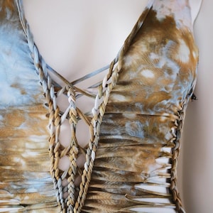 Peut inclure: Un haut tie-dye dans les tons de bleu, marron et blanc. Le haut présente un col en V profond avec un design tressé et entrecroisé et des détails découpés sur les côtés. Le tissu a un aspect texturé.