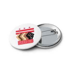 Puede incluir: Botón blanco con un diseño que presenta rayas y estrellas rojas, con una serie de puños estilizados en varios tonos de piel, y el texto "FREE DC" en rojo. El botón es una declaración política.