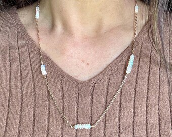 May include: A delicate gold chain necklace with multiple small white opal beads. The necklace features a cluster of beads in the center and smaller clusters at the top and bottom.