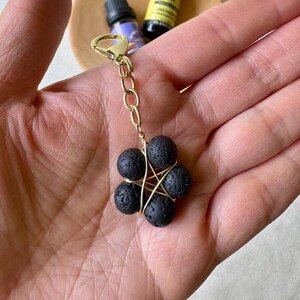 May include: A gold-colored keychain with a cluster of six black lava rock beads. The beads are held together with gold-colored wire, forming a star-like shape. The keychain has a lobster claw clasp.