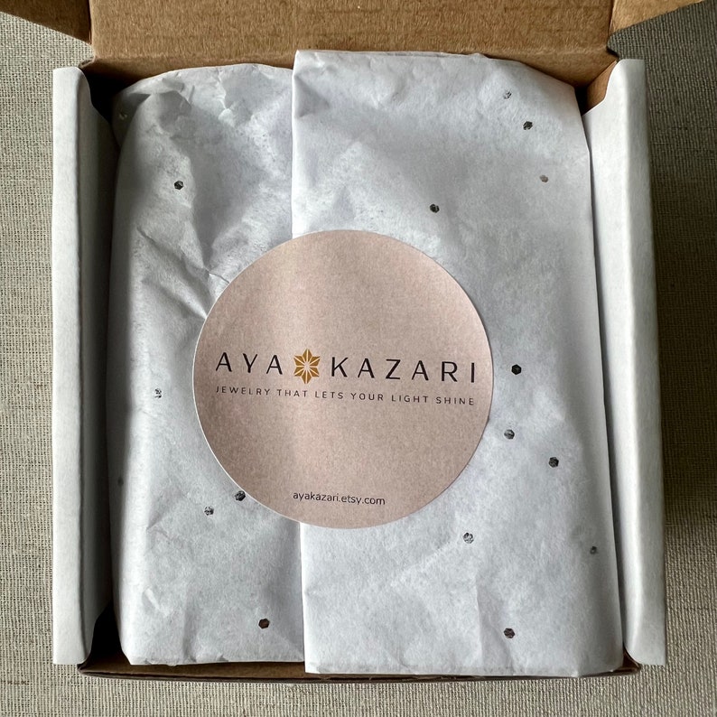 May include: A white box with a white tissue paper lining. The tissue paper has a small, round sticker with the text "AYA KAZARI JEWELRY THAT LETS YOUR LIGHT SHINE ayakazari.etsy.com".