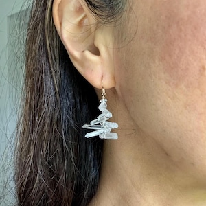 May include: A pair of gold earrings with clear quartz crystals hanging from them. The crystals are arranged in a cascading, asymmetrical design.