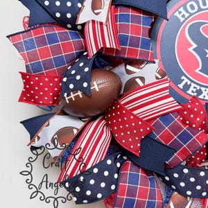 May include: A decorative wreath featuring a circular sign with the text HOUSTON TEXAS, accented with ribbons in red, white, and blue patterns including polka dots, stripes, and plaid, interspersed with small brown football-shaped ornaments.