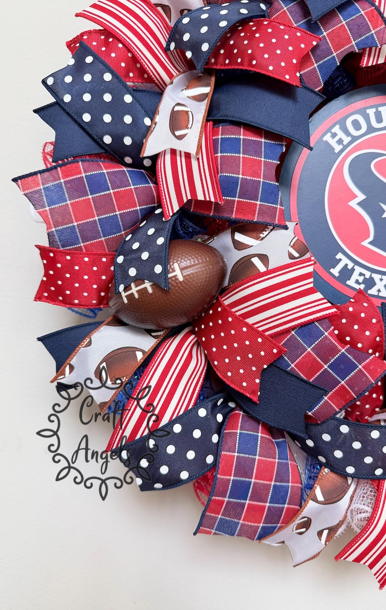 May include: A decorative wreath featuring a circular sign with the text HOUSTON TEXAS, accented with ribbons in red, white, and blue patterns including polka dots, stripes, and plaid, interspersed with small brown football-shaped ornaments.