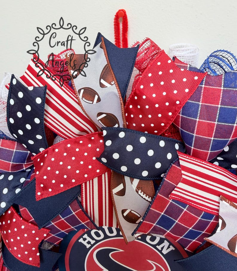 May include: A decorative wreath featuring red, white, and blue ribbons with polka dot, striped, and plaid patterns. Some ribbons display a football graphic. A circular sign with the text HOUSTON is visible at the bottom, and a red pipe cleaner hanger.