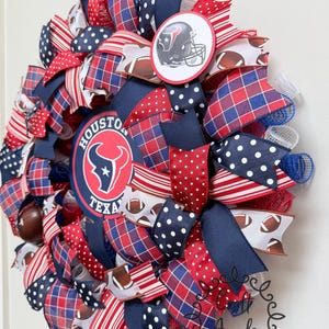 May include: A decorative wreath featuring the Houston Texans logo and a football helmet graphic. The design incorporates red, white, and blue ribbons with polka dot, plaid, and striped patterns, interspersed with mesh and small football motifs.