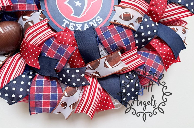 May include: A decorative wreath featuring a central Houston Texans logo sign surrounded by ribbons in red, white, and navy blue. The ribbons display patterns including red and blue plaid, white polka dots on navy, red stripes, and football graphics.