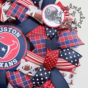 May include: A decorative wreath featuring Houston Texans branding with a large circular logo and a smaller football helmet emblem. The design incorporates ribbons in red, white, and navy blue with patterns including polka dots, plaid, stripes, and footballs.
