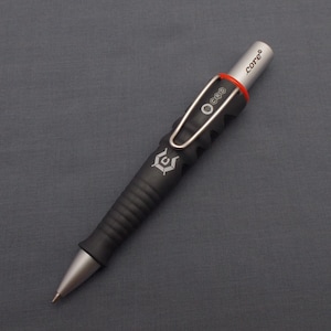 May include: A black and silver pen with a textured grip and a red rubber band. The pen has a silver clip and the word "core" is engraved on the top of the pen.