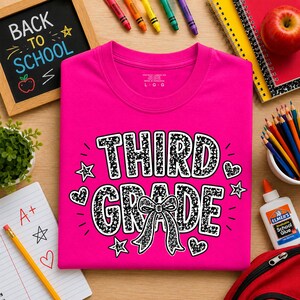 Può includere: Una t-shirt rosa acceso con la scritta THIRD GRADE in un carattere nero e bianco maculato. Il design include un fiocco centrale, diverse piccole stelle e cuori. La maglietta ha un girocollo ed è di taglia large, come indicato sull'etichetta.