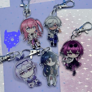 May include: Five colorful anime character keychains with silver key rings. The characters are drawn in a chibi style and feature different hairstyles, clothing, and accessories.