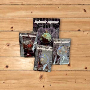 May include: Four enamel pins featuring colorful cartoon characters with the text "Black Moon" on each card. The characters are a green and brown creature, a red and black creature, a blue and purple creature, and a blue and green creature.