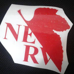 May include: A white sticker with a red leaf design and the word "NERV" in red letters.