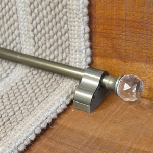 May include: A close-up of a metal stair rod with a crystal finial. The rod is attached to a wall and is part of a stair railing system.