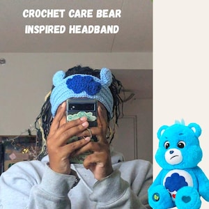 May include: A blue crocheted headband inspired by Care Bears. The headband features a blue cloud with a white outline and a white heart in the center. The headband is worn by a person with long, dark hair.