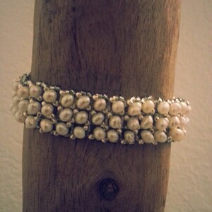 May include: A white pearl bracelet with a woven design. The bracelet is displayed on a piece of driftwood.