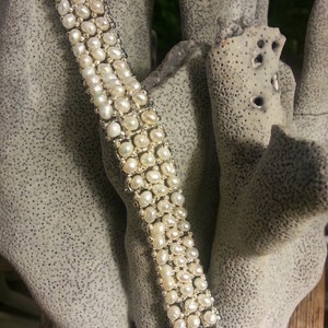 May include: A white pearl bracelet with multiple rows of pearls. The bracelet is made of small, round pearls that are strung together on a silver chain.