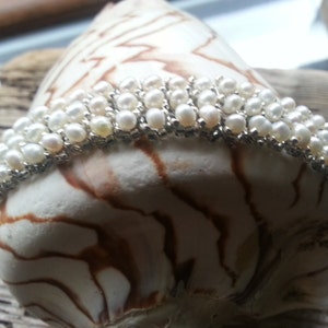 May include: A white pearl bracelet with silver accents. The bracelet is made of multiple rows of pearls and is displayed on a seashell.