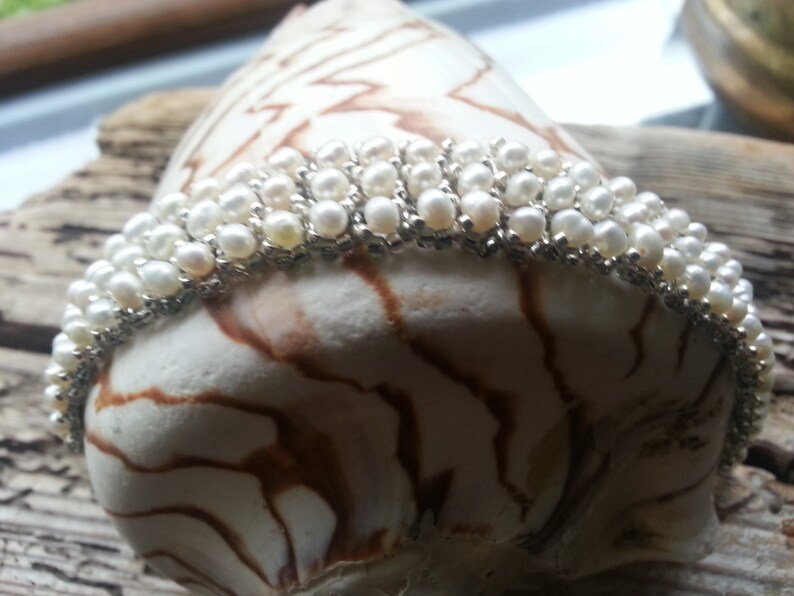 May include: A white pearl bracelet with silver accents. The bracelet is made of multiple rows of pearls and is displayed on a seashell.